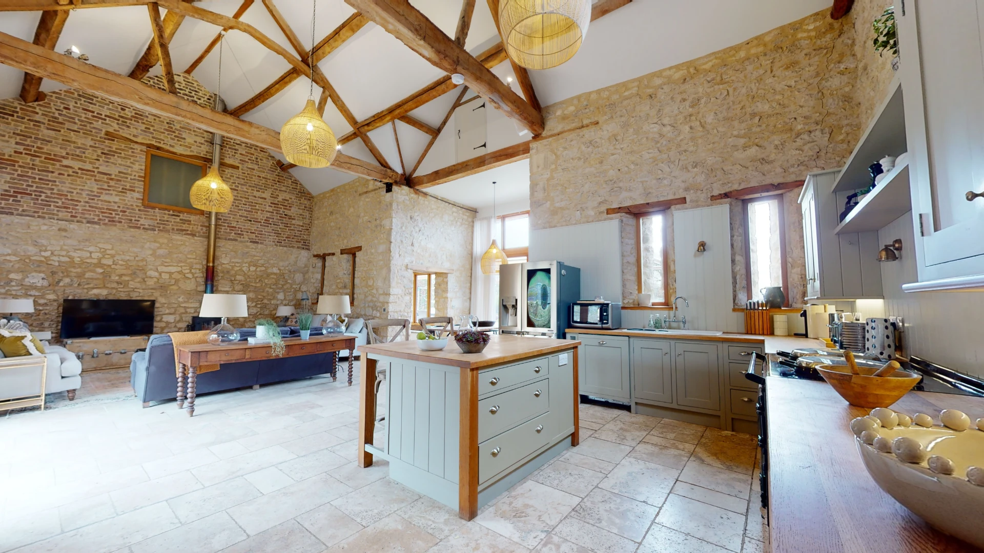 Stone Barn open-plan living space with exposed A-frame trusses, bare stone walls and a pale green kitchen island