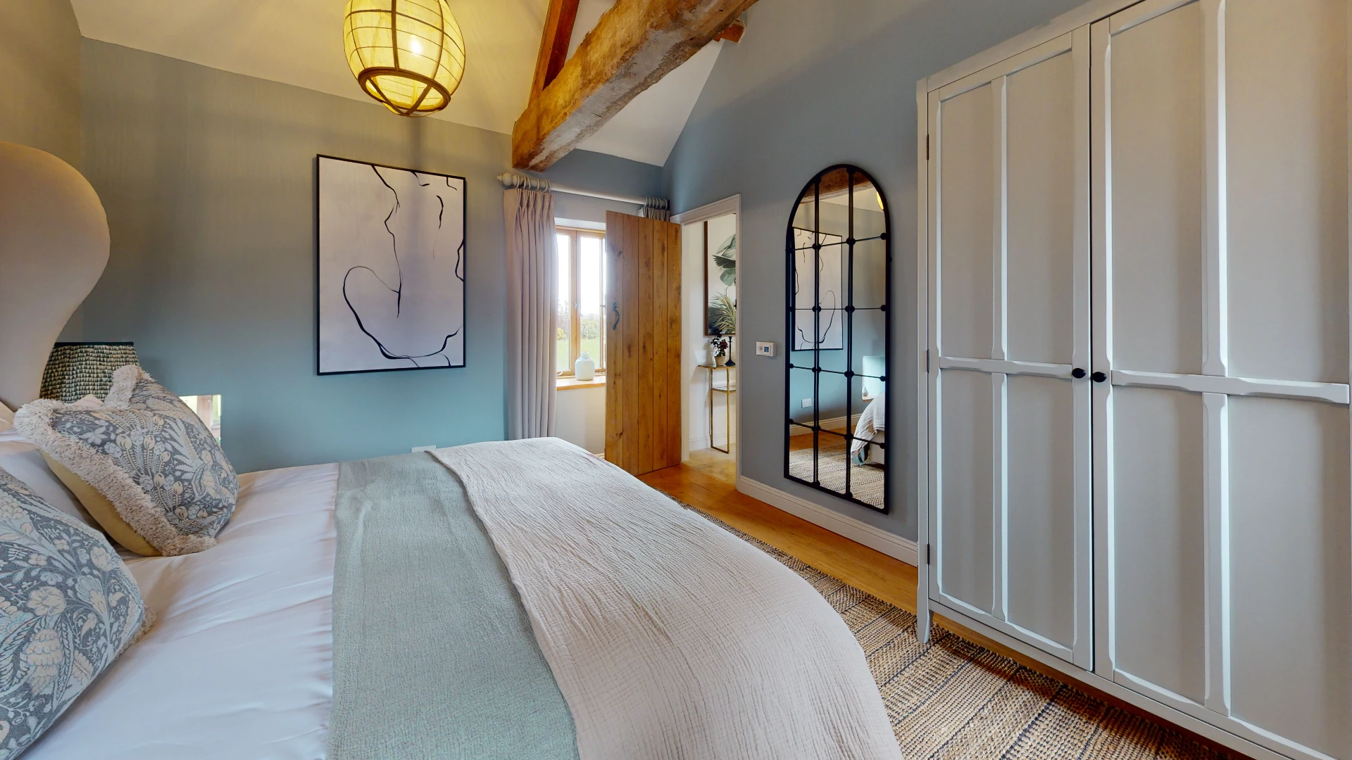 Stone Barn bedroom with a soft blue feature wall, exposed beams and fitted wardrobes