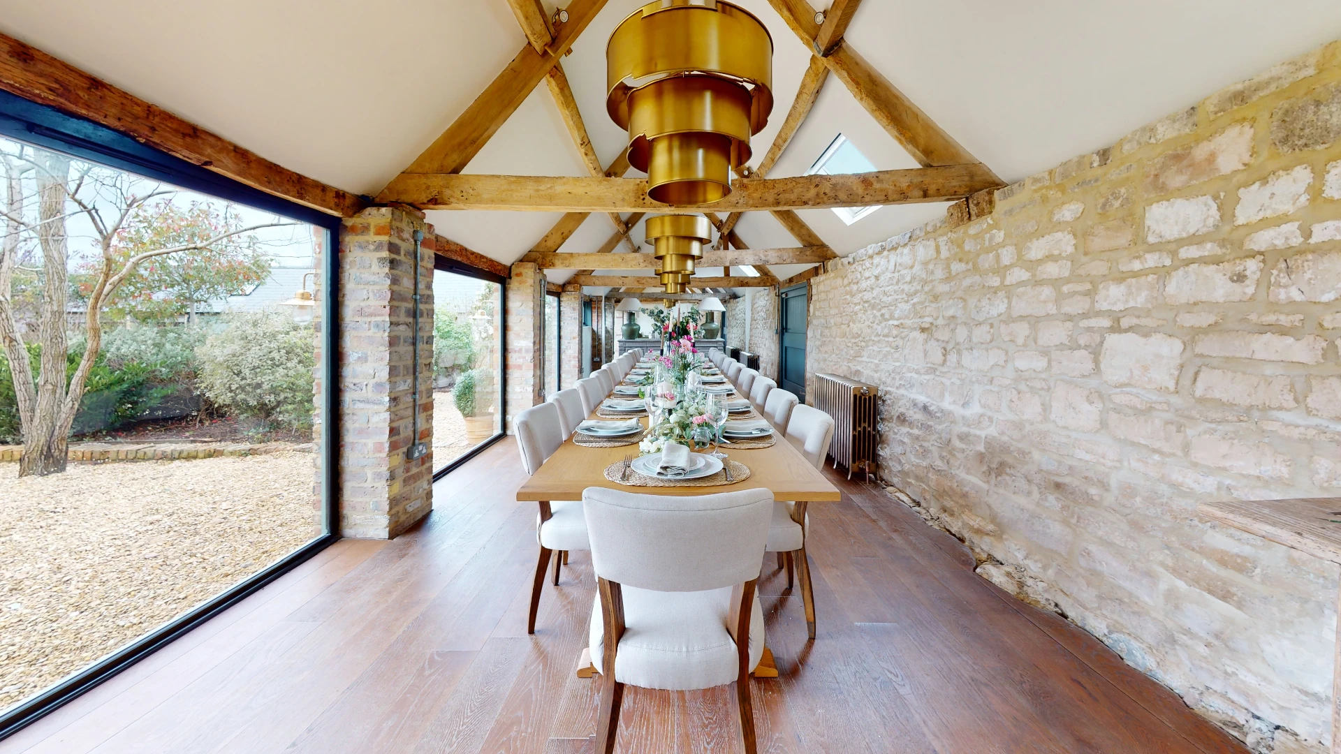 Stone Barn banqueting table set for a wedding under an exposed oak truss and a brass pendant light