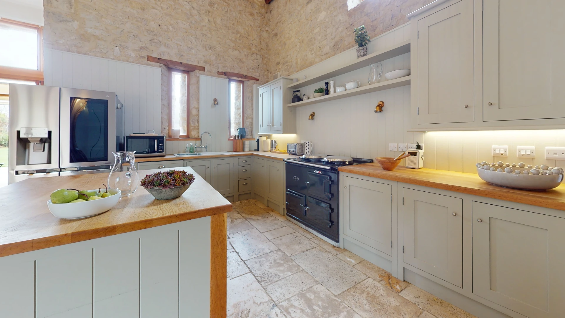 Stone Barn kitchen with sage shaker units, oak worktops and a cream range cooker against a bare stone wall