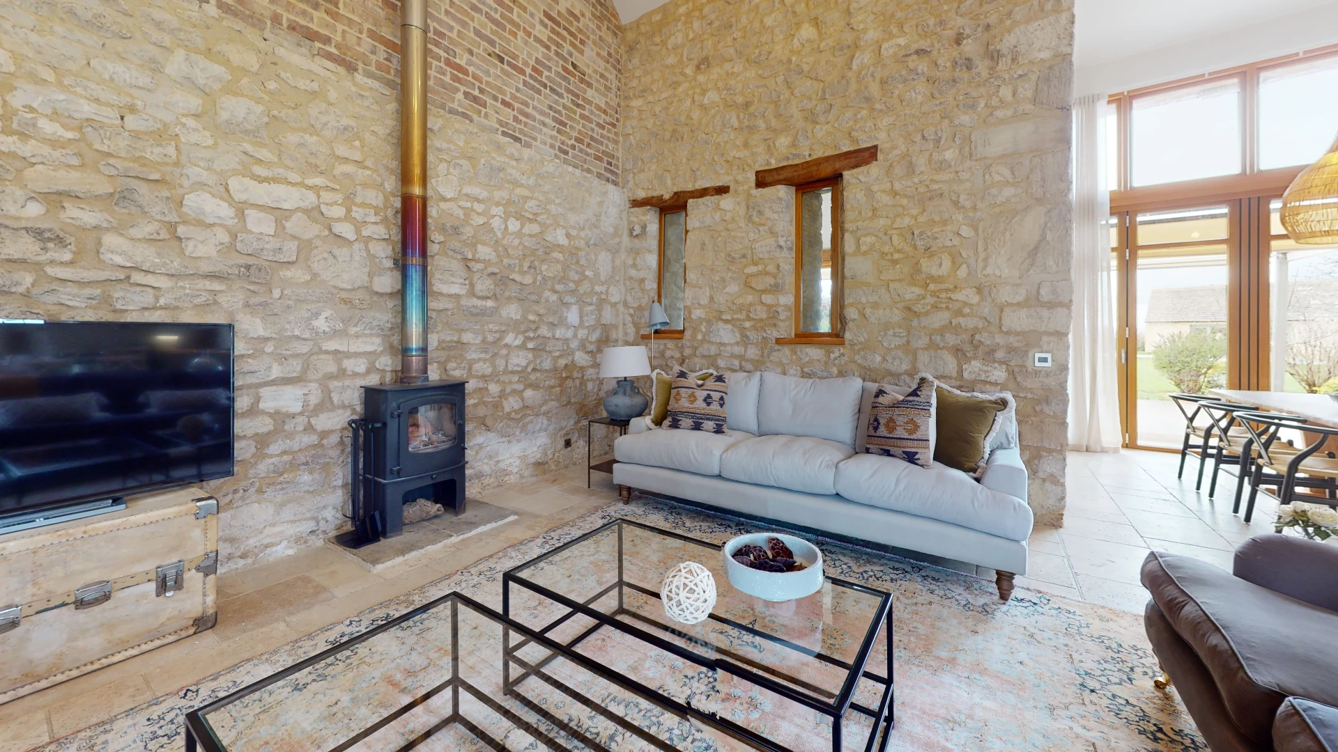 Stone Barn living room with a wood burning stove set into bare stone, a grey sofa and a wall-mounted television