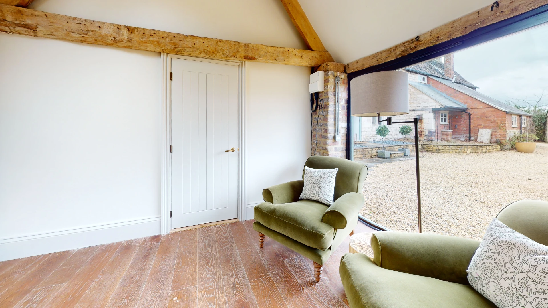 Stone Barn snug with green velvet armchairs and glazed doors opening onto the gravel courtyard